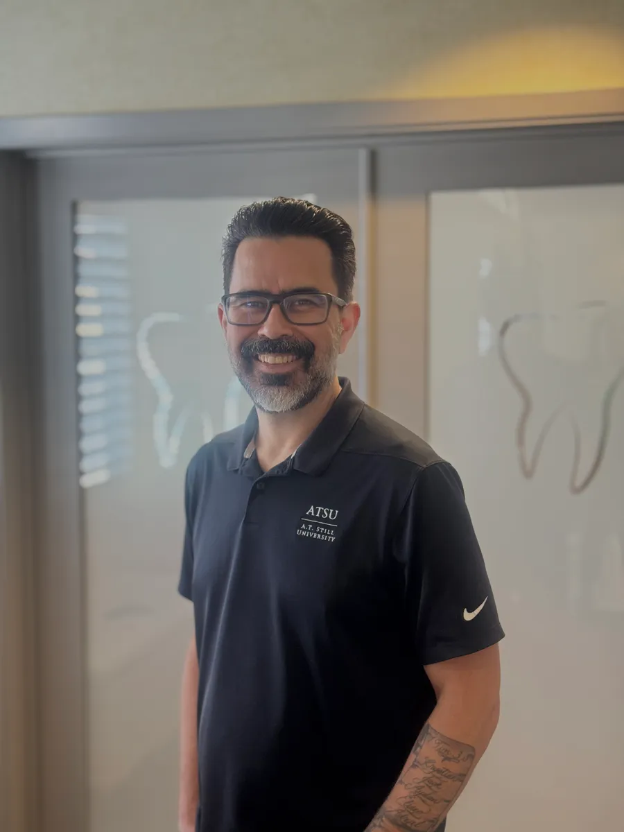 Dr. Isaac Navarro smiling in a hallway at Navarro Dentistry in Visalia, wearing a navy A.T. Still University polo